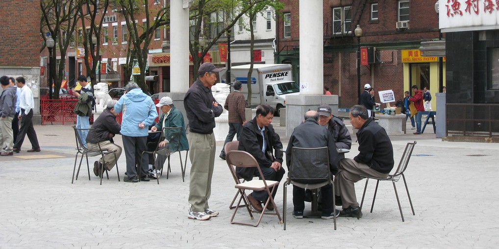 Older adults, chatting at outdoor tables. 