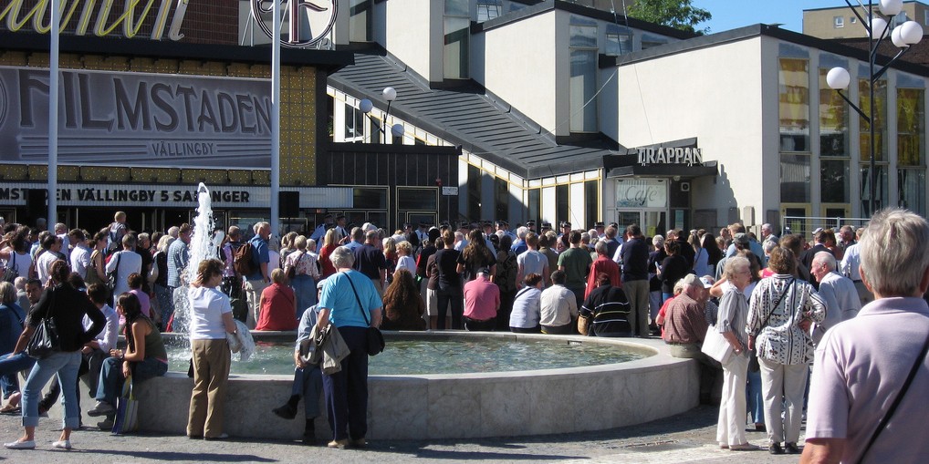 Large gathering of people outside of movie theater near fountain. 