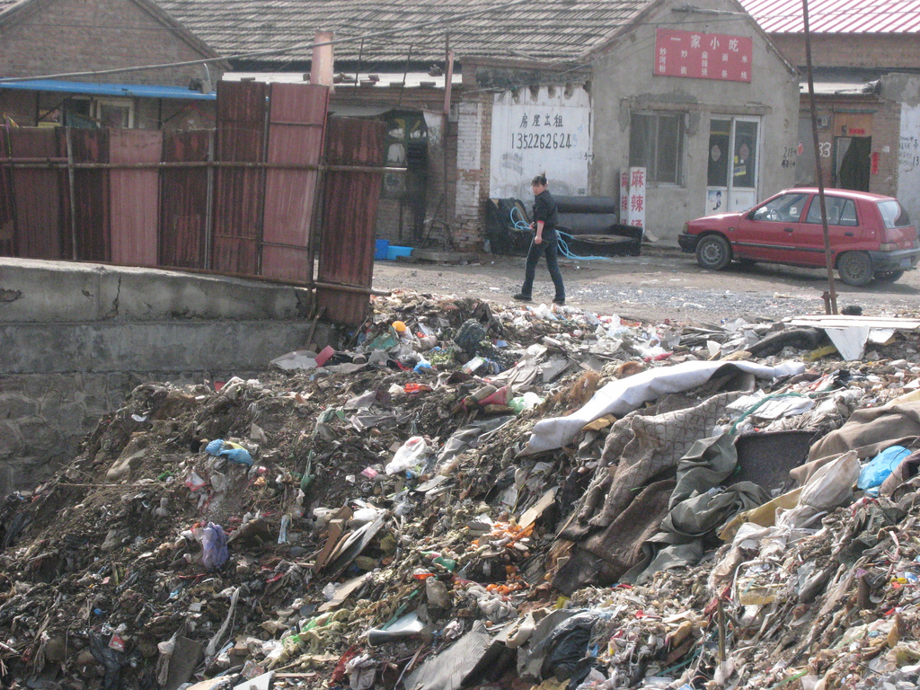 Large mound of trash, next to road and store. 