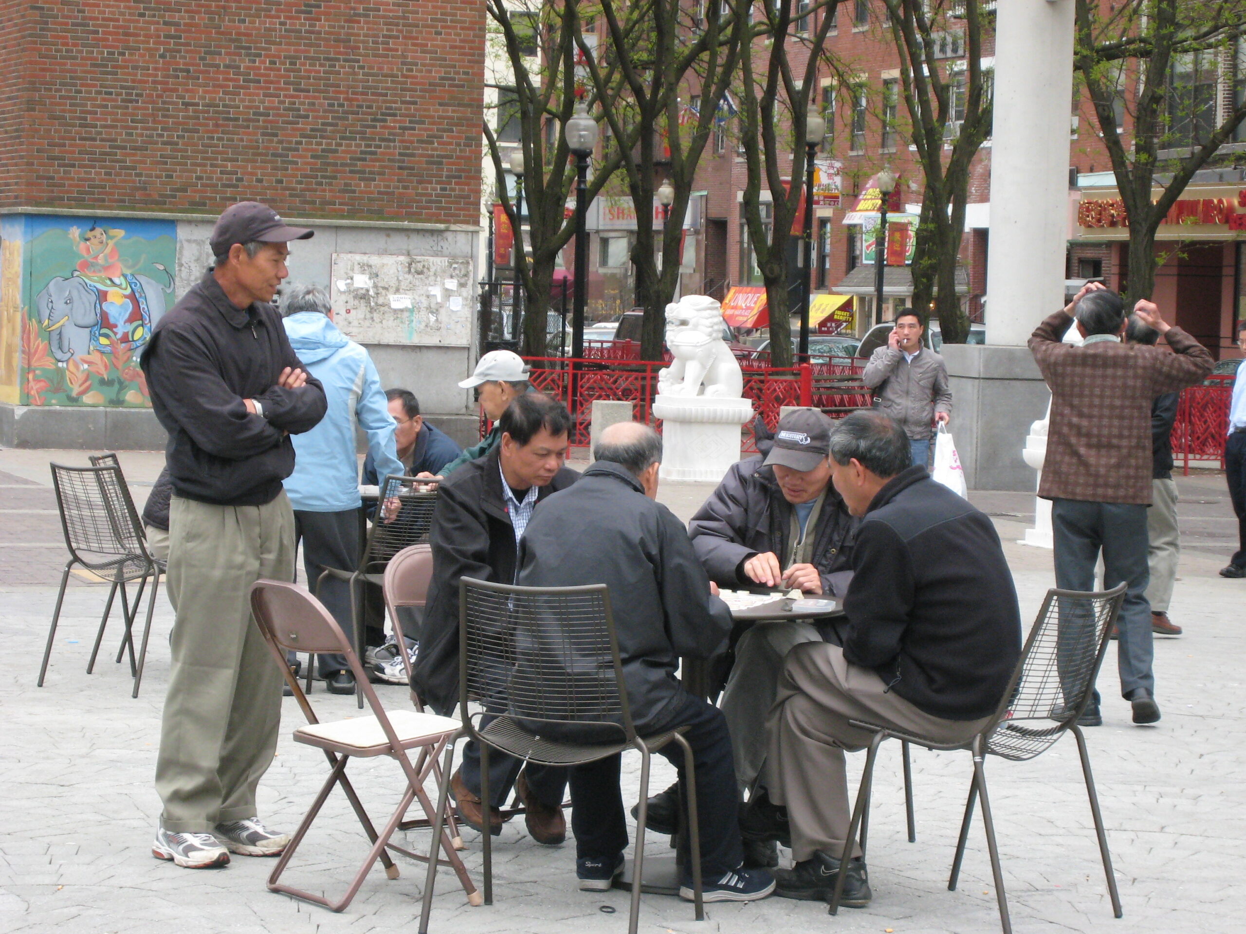 Adults, playing game at outdoor table in plaza.