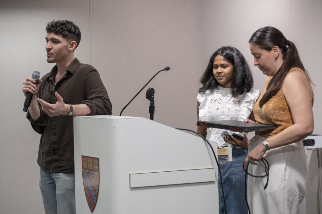 Miriam and Gemrisha at a podium, Enrique holding a microphone, mid-conversation