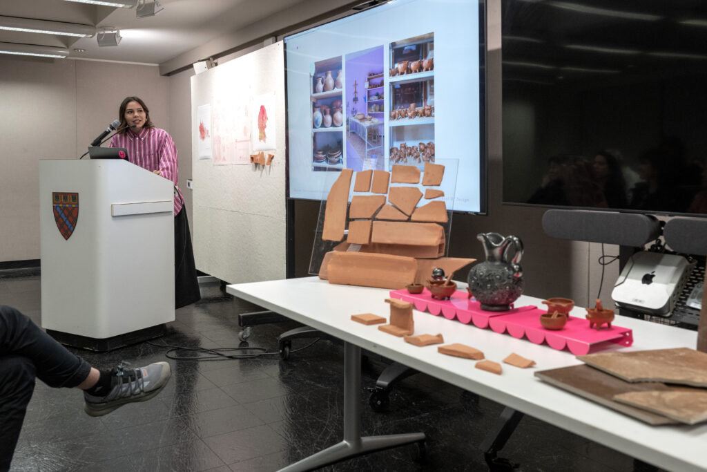 Andrea at a podium with ceramic artifacts and printed materials laid out on a table
