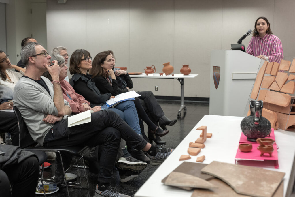 Speaker at a podium with ceramic artifacts and printed materials laid out on a table