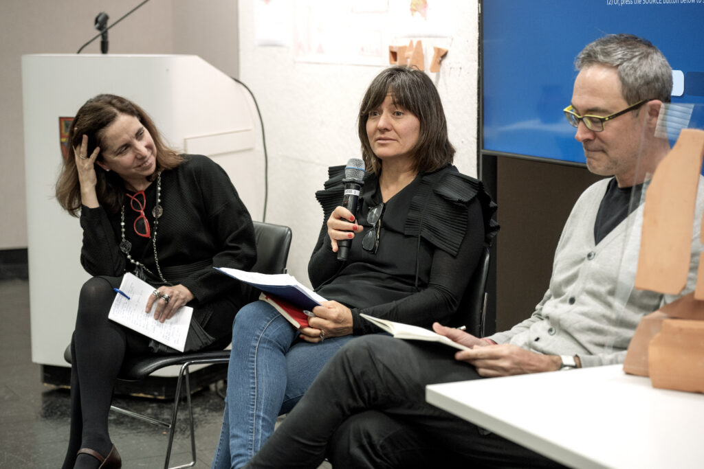 Two panelists seated at a table, Laura Janka speaking into a microphone