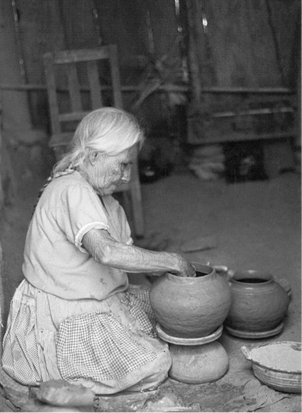 Black-and-white photo of a woman shaping clay on a table